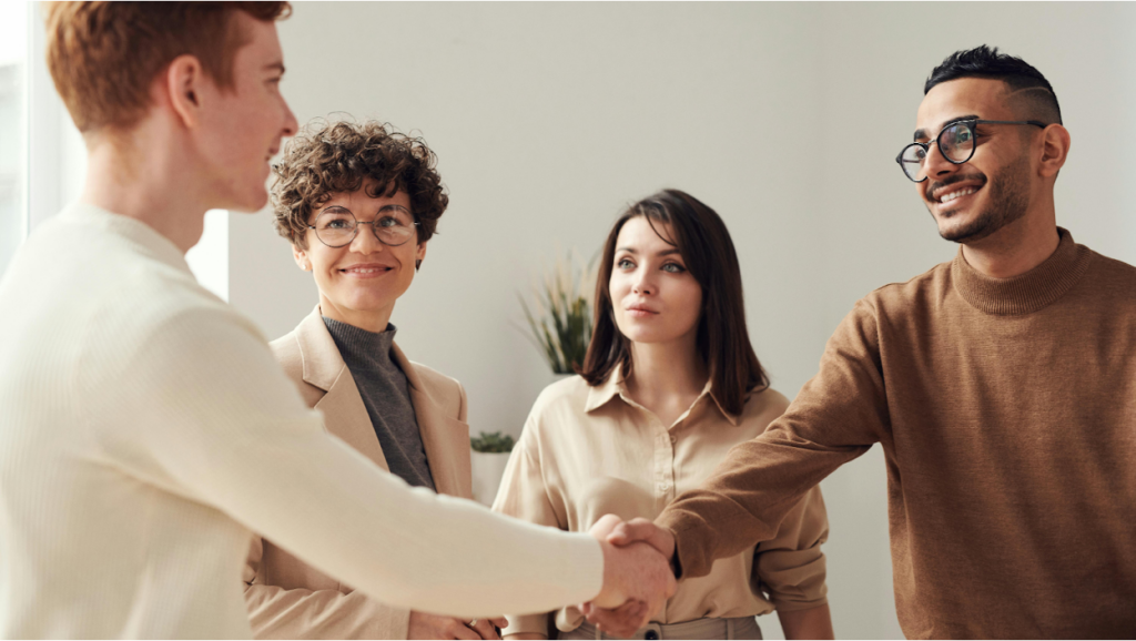 Four professionals in business casual attire during a handshake meeting in a modern office with neutral tones.