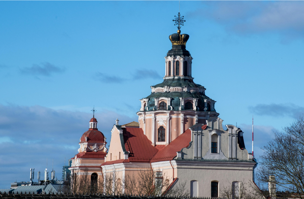 Historic church with ornate pink tower, dark crown, and red terracotta roof against blue sky