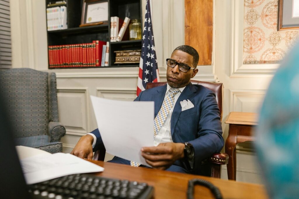 A man in a blue suit reviews documents at a desk.