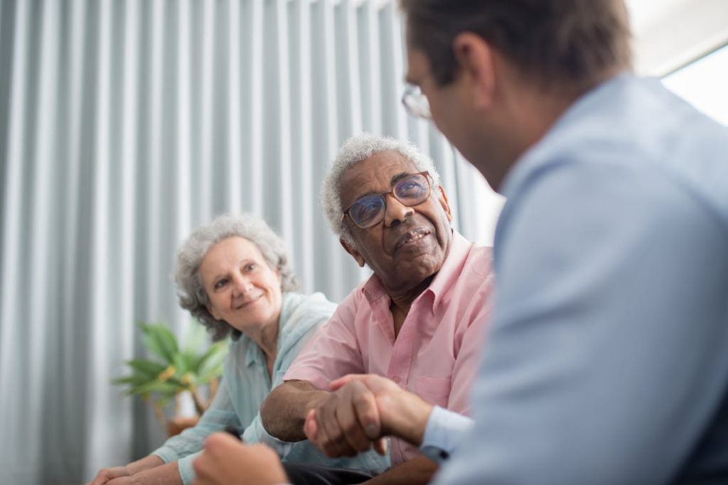 Financial advisor meeting with two elderly clients reviewing documents at a table.