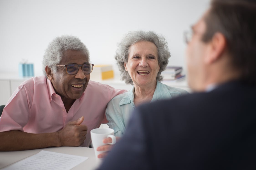 A man discussing documents with an elderly couple at a table with a laptop and paperwork.