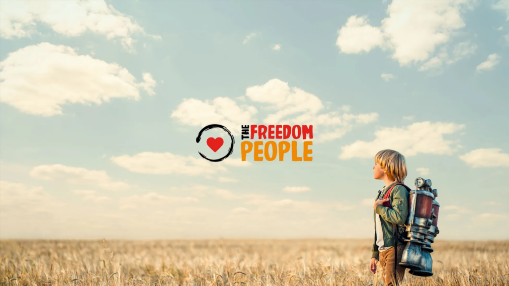 Young person with backpack standing in golden field under blue sky with The Freedom People logo.