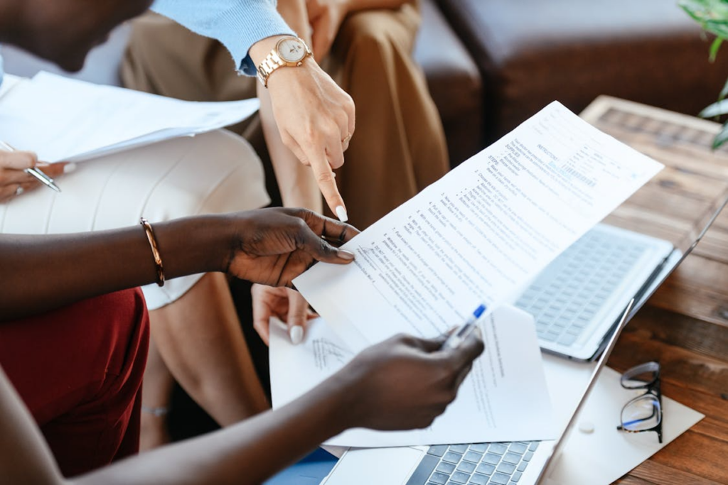 A businesswoman holding a blue pen and checking a document while another person is pointing at the document