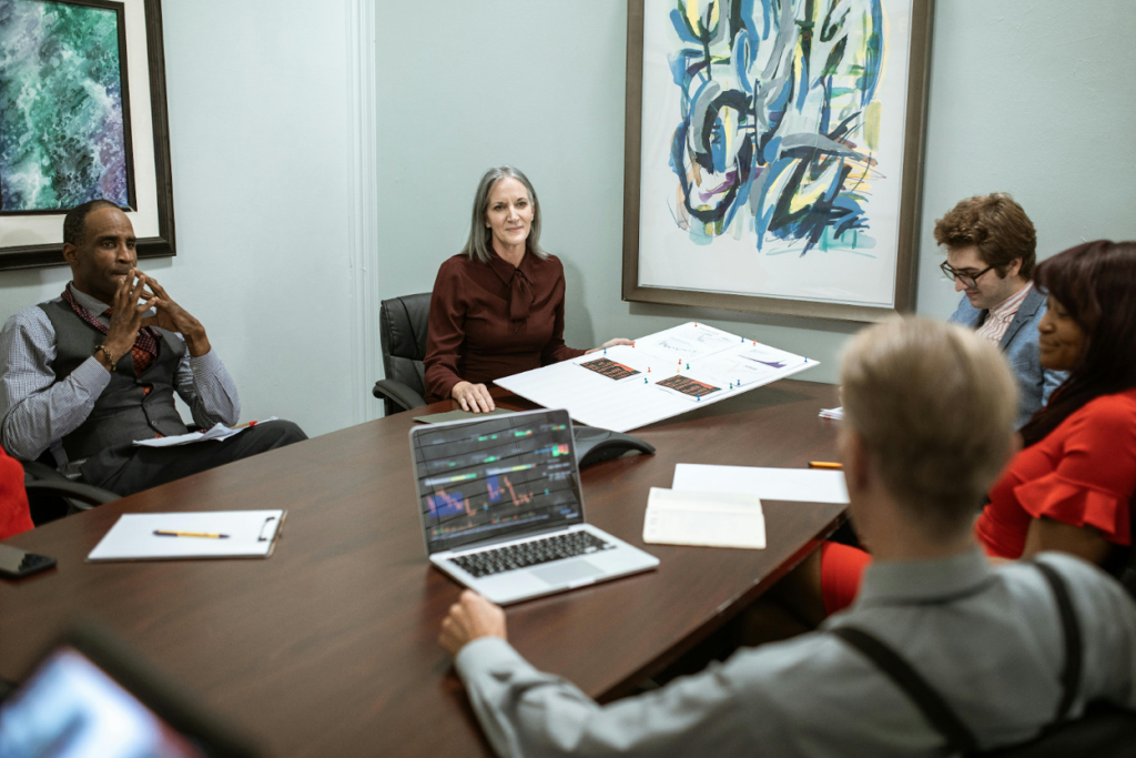A group of professionals in a conference room meeting with a laptop and documents on the table