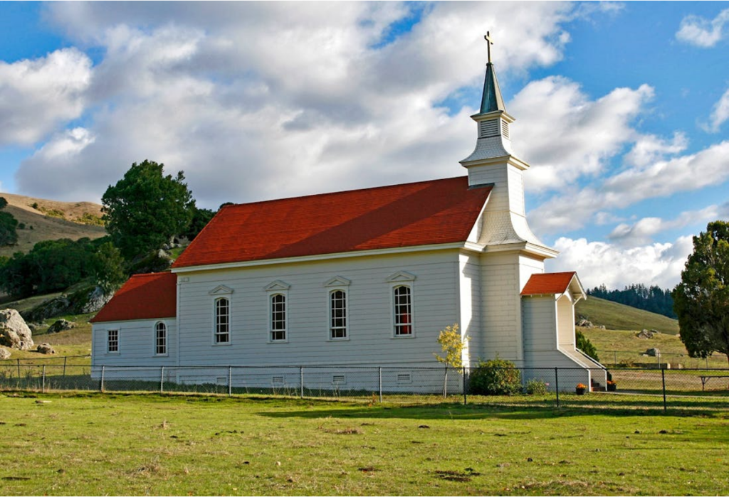 A rural red and white concrete church on green grass field, representing the type of religious organization that may qualify under Section 508(c)(1)(A)