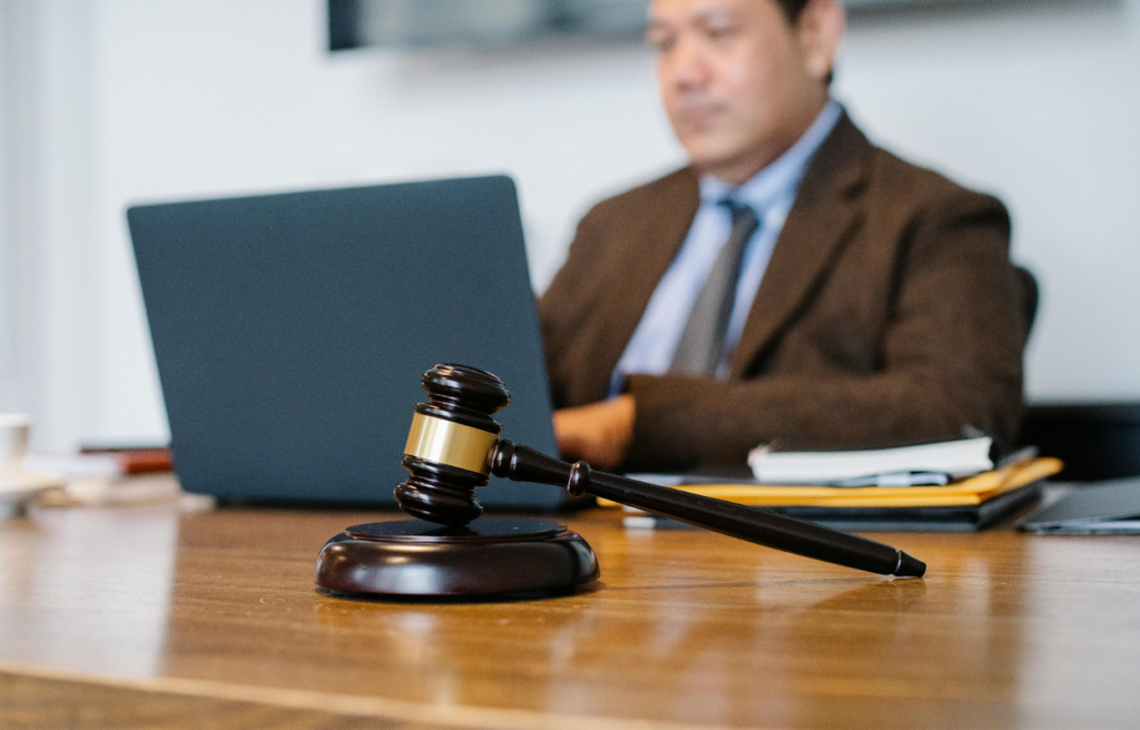 A wooden gavel on a desk with a person in a suit working on a laptop in the background