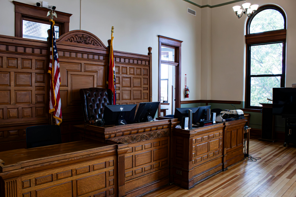 Empty courtroom with ornate wooden judge's bench, American flag, leather chair, and arched windows