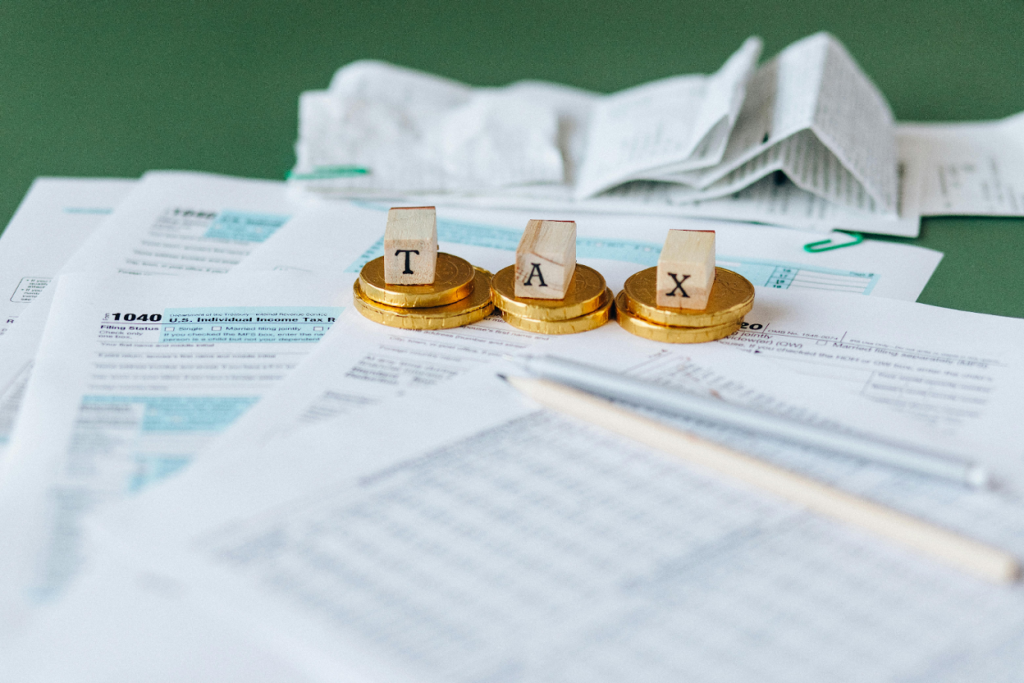 Wooden letter blocks spelling "TAX" on gold coins atop IRS 1040 tax forms with a pen