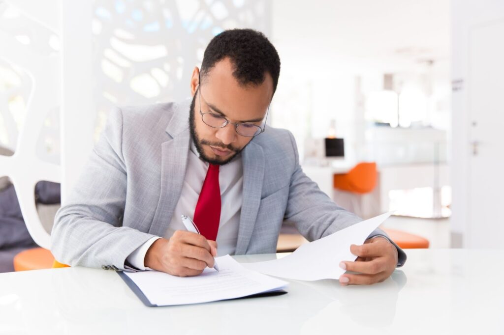 Business owner signing trust documents with a pen while seated at a conference table with legal folders and paperwork.