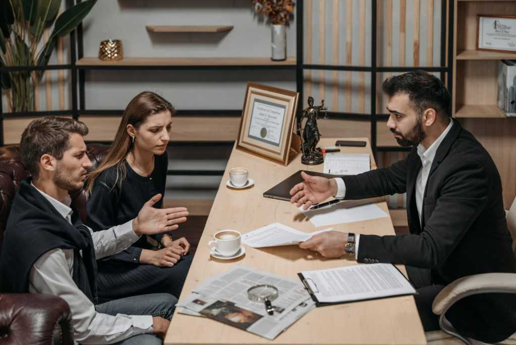 A couple consulting with a professional at a desk with documents, coffee, and a Lady Justice statue.
