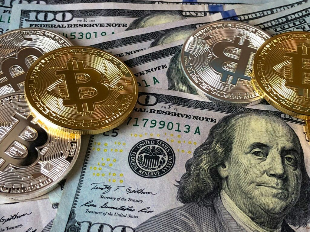 Gold Bitcoin coins scattered on top of US hundred-dollar bills