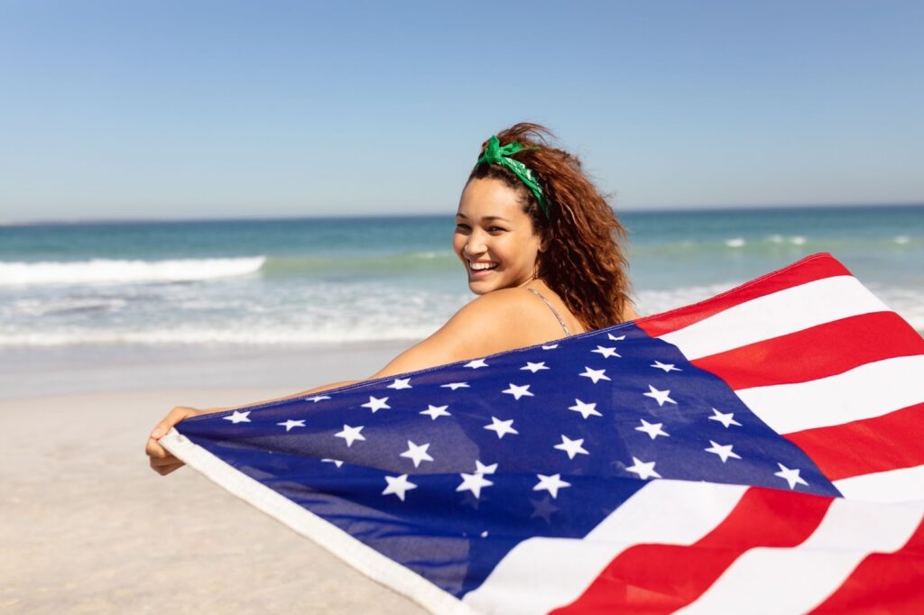 Woman holding an American flag on a sunny beach.