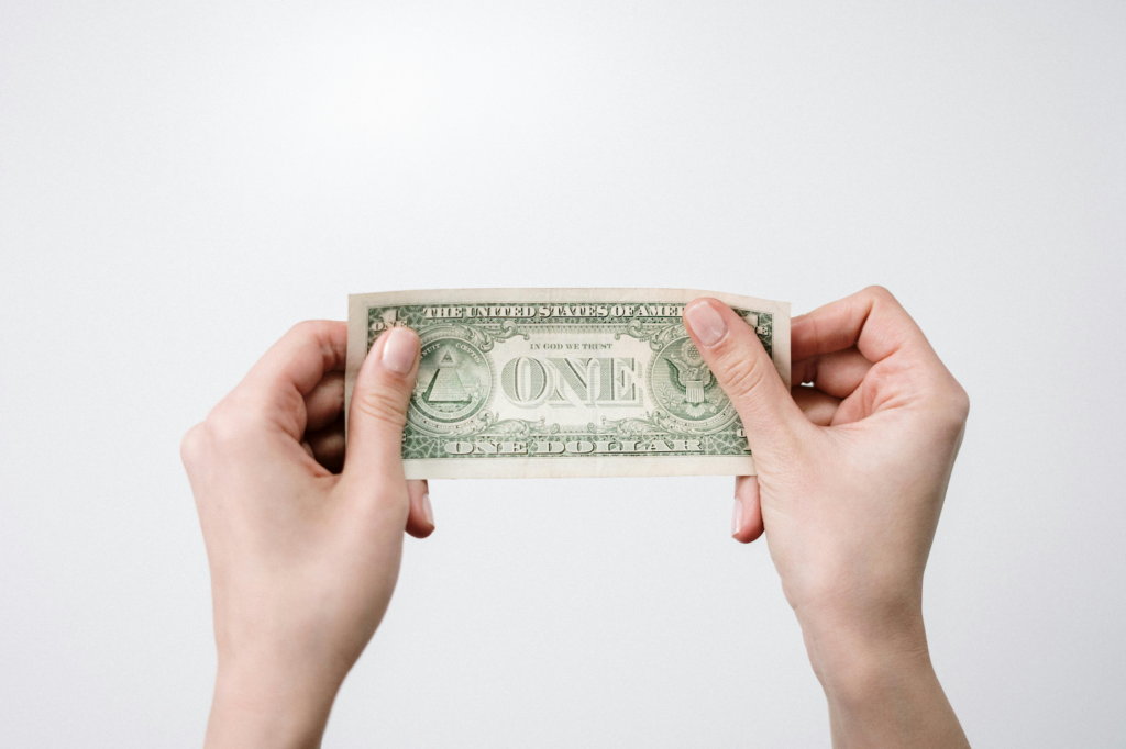 Two hands holding a US one-dollar bill against a white background.