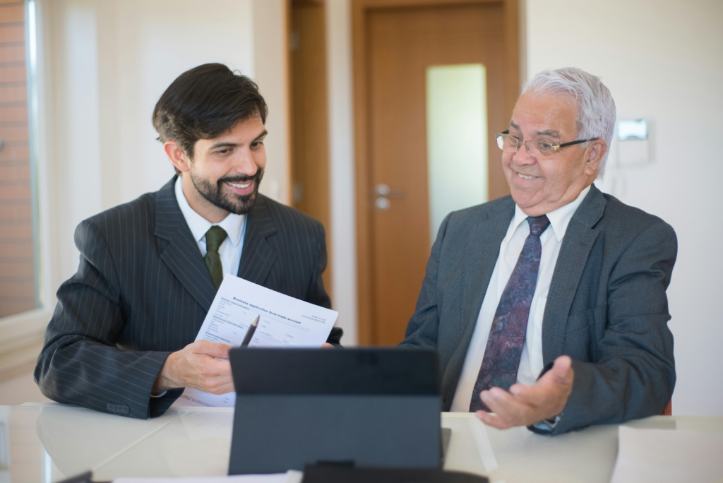 Two businessmen in suits smiling while reviewing a business application form at a desk.