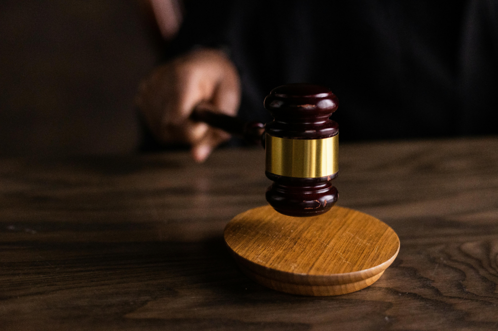 A judge's hand striking a wooden gavel on a sound block in a dark courtroom setting.
