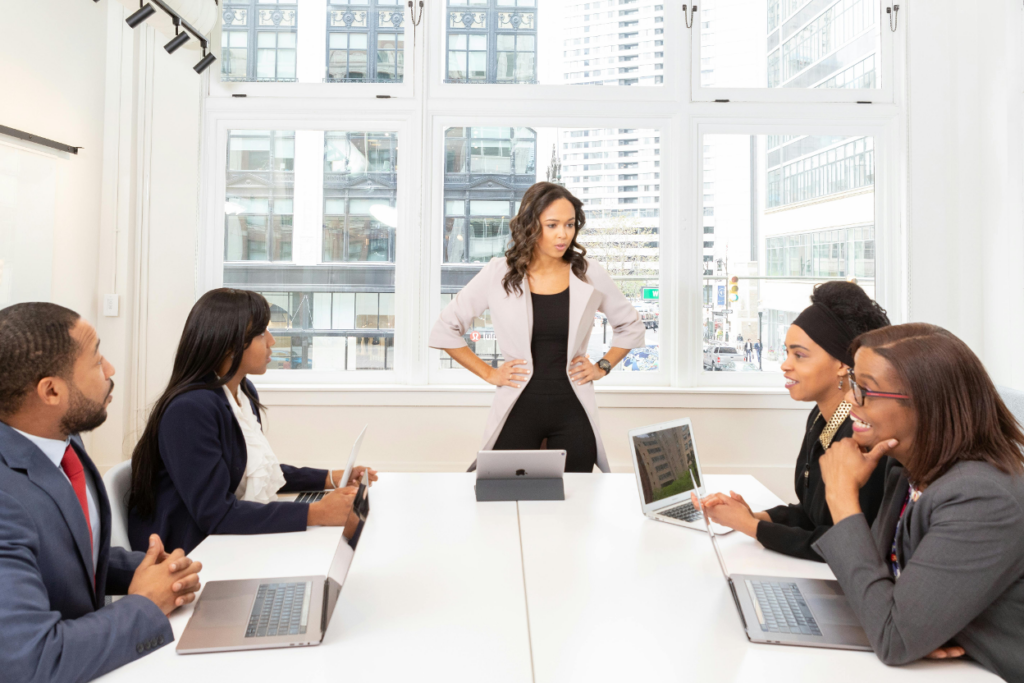 A woman leads a meeting with four colleagues at a conference table in a bright office