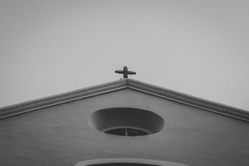 Black-and-white low-angle view of a church rooftop with a cross and circular window