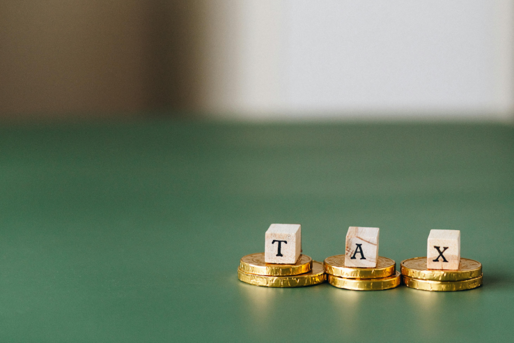 Wooden blocks spelling "TAX" placed on stacks of gold coins against a green background