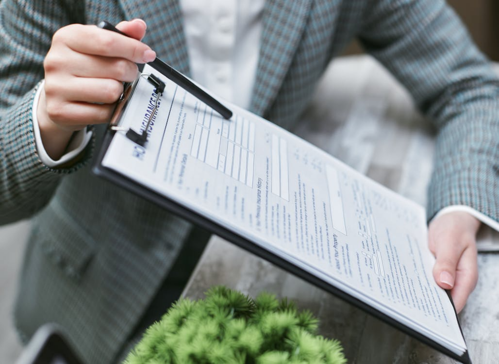Person in a plaid blazer holding a clipboard with a form and a pen.