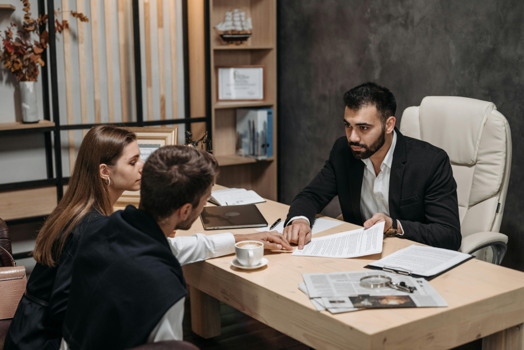 A professional man in a suit presents documents to a couple across an office desk.