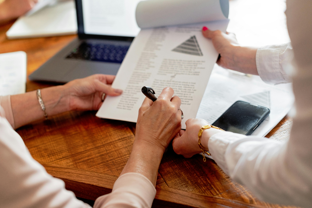 Two people reviewing a document with charts at a wooden desk near a laptop.