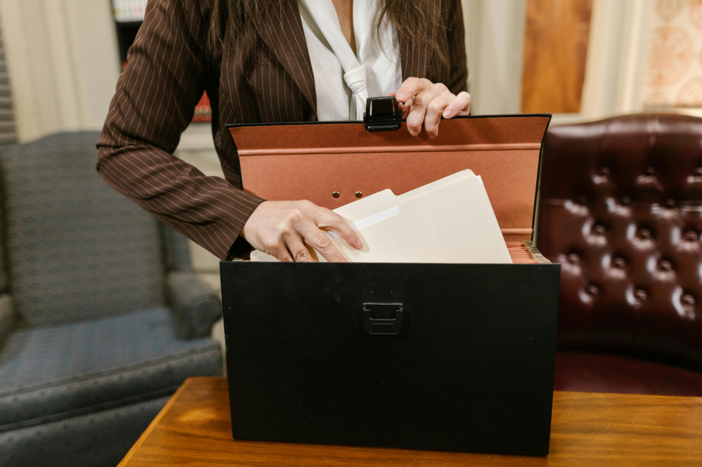 Woman in a pinstripe blazer organizing file folders inside a black document storage box on a wooden table.