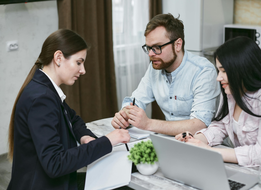 Three professionals review documents and a laptop together at a desk during a business meeting.