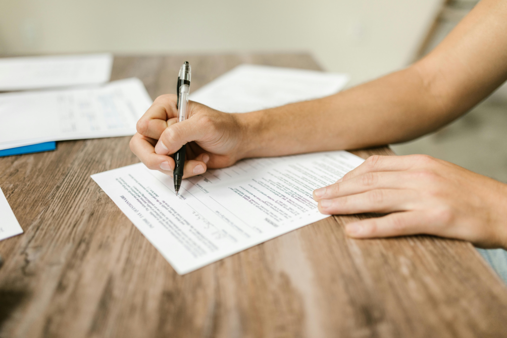 A person fills out a tax questionnaire form on a wooden desk with a black pen.