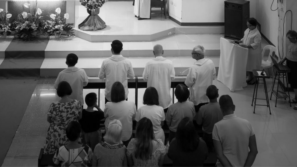 Black and white photo of people kneeling in prayer during a church service near the altar.