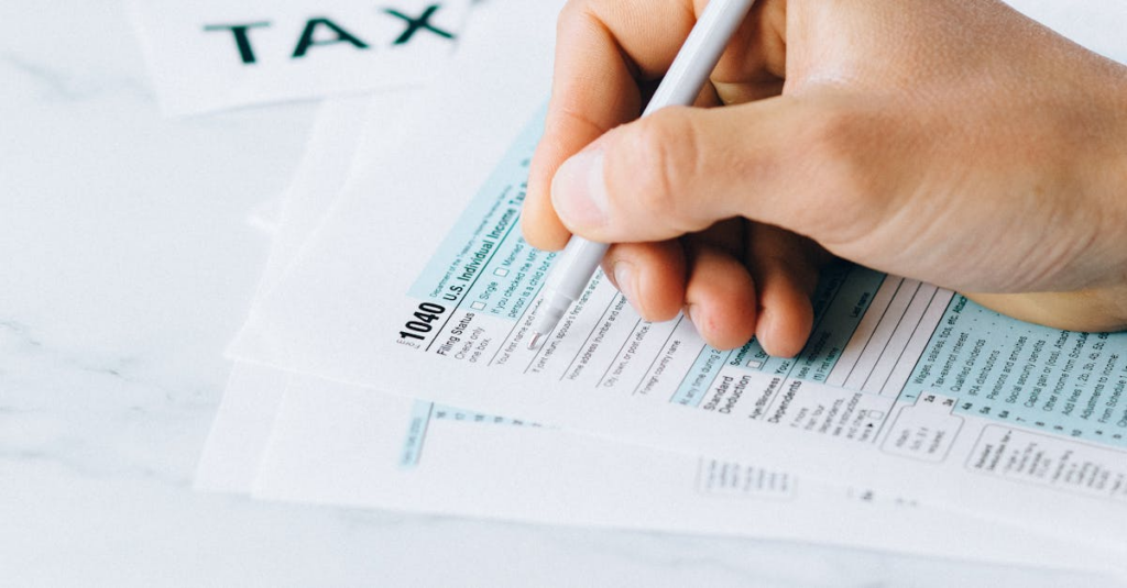 A hand holding a pen filling out a tax return form.