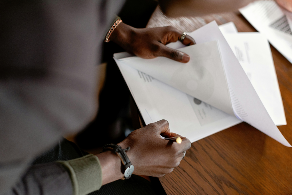 Close-up of hands holding and reviewing printed documents over a wooden desk.