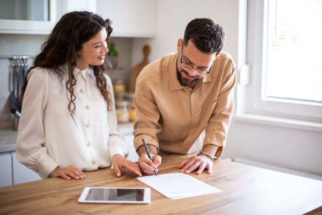 Couple jointly signing family business paperwork at their kitchen counter, illustrating shared ownership decisions