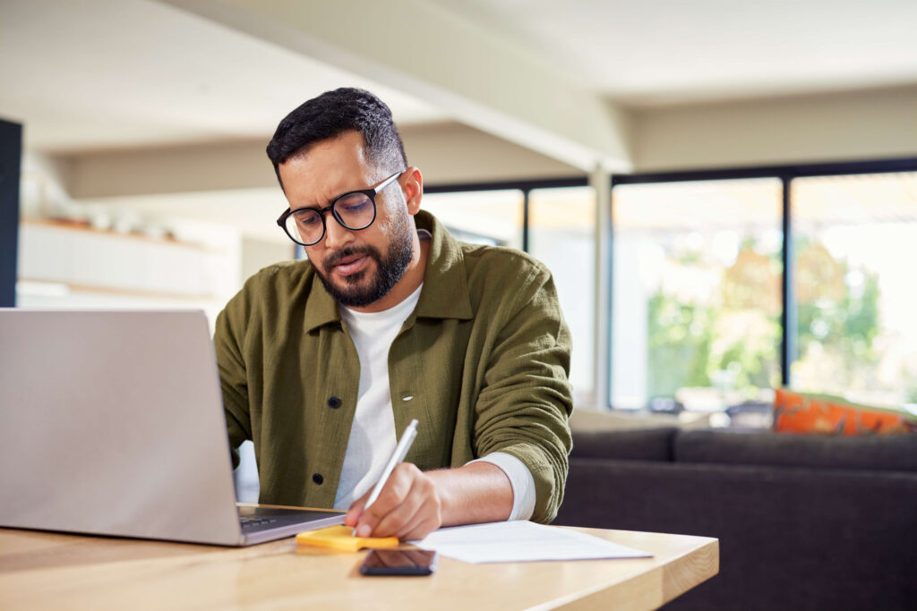Man in glasses reviewing financial documents at his laptop, working through nonprofit tax filing paperwork