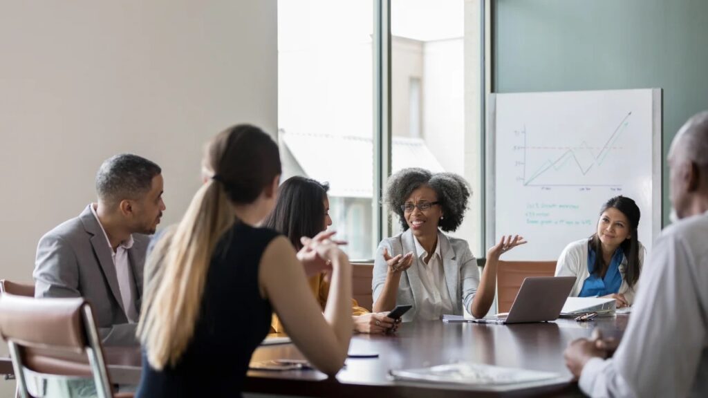 Non-profit board members in a strategy meeting, as a leader presents growth charts on a whiteboard