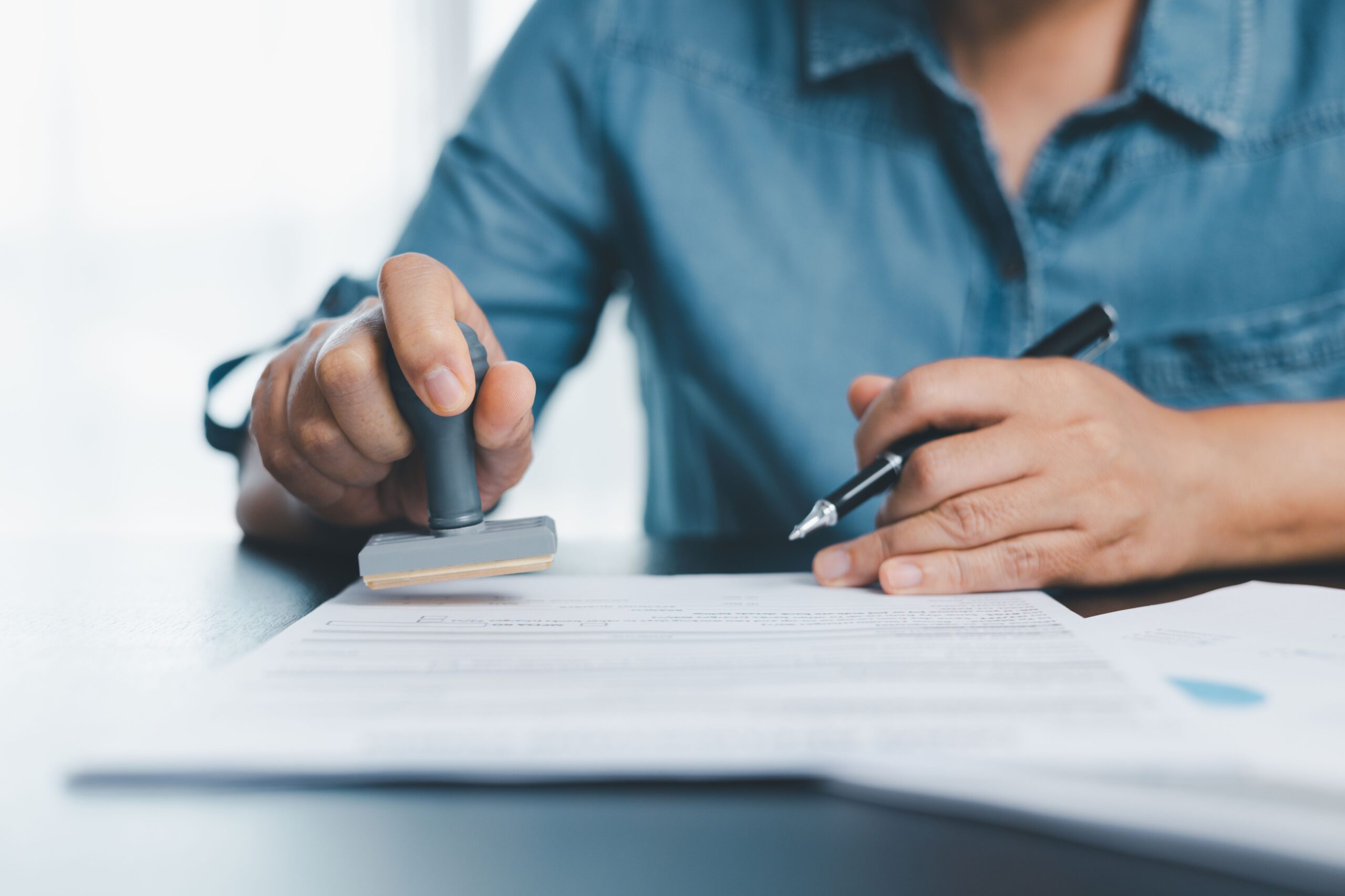 Person in a blue shirt stamping and signing official tax documents at a desk, representing nonprofit compliance paperwork