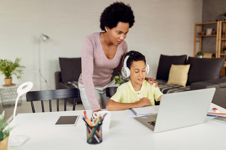 Mother guiding her headphone-wearing son through an online lesson at home, illustrating a private homeschool learning setup.