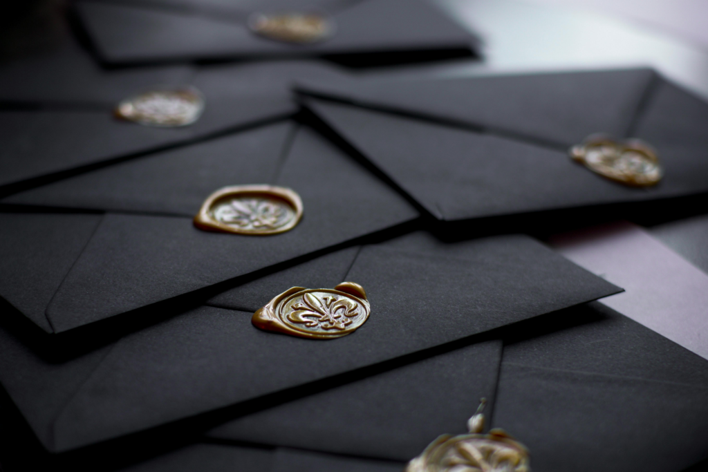 Black envelopes sealed with ornate gold wax stamps arranged on a flat surface.