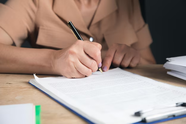 Hand signing paperwork beside stacked documents, reflecting the written agreements and recordkeeping that protect a PMA's legal standing.
