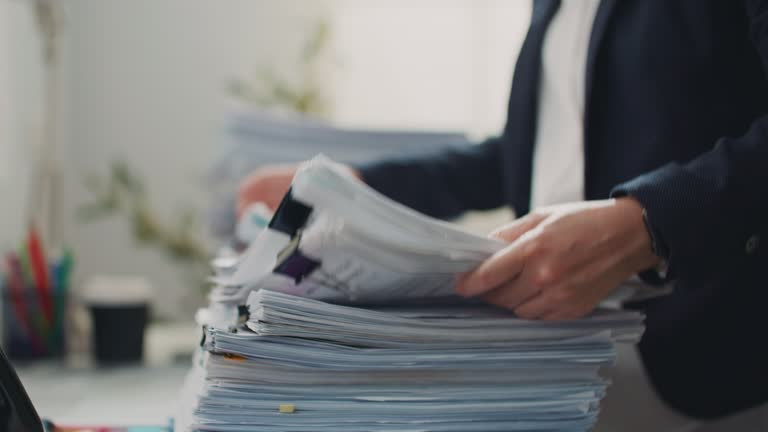 Administrator sorting tall stacks of paperwork on a desk, illustrating the Form 990 and recordkeeping demands of nonprofit tax compliance.
