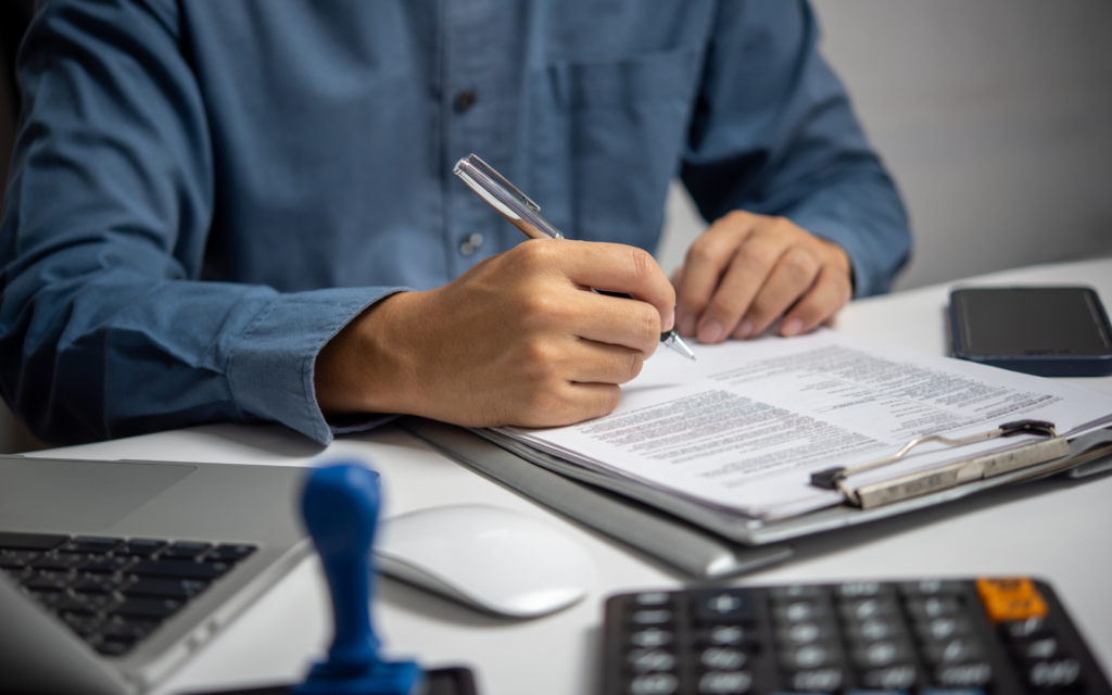 Nonprofit administrator signing 501(c)(2) compliance paperwork at a desk with a calculator and laptop.
