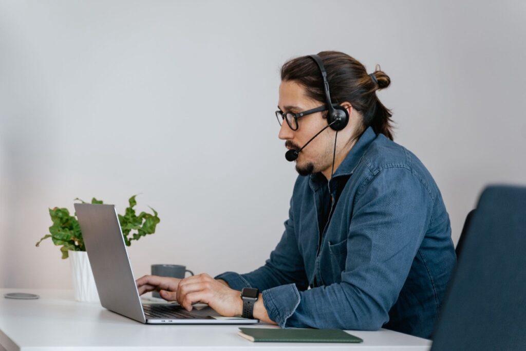 A consultant wearing a headset and glasses types on a laptop