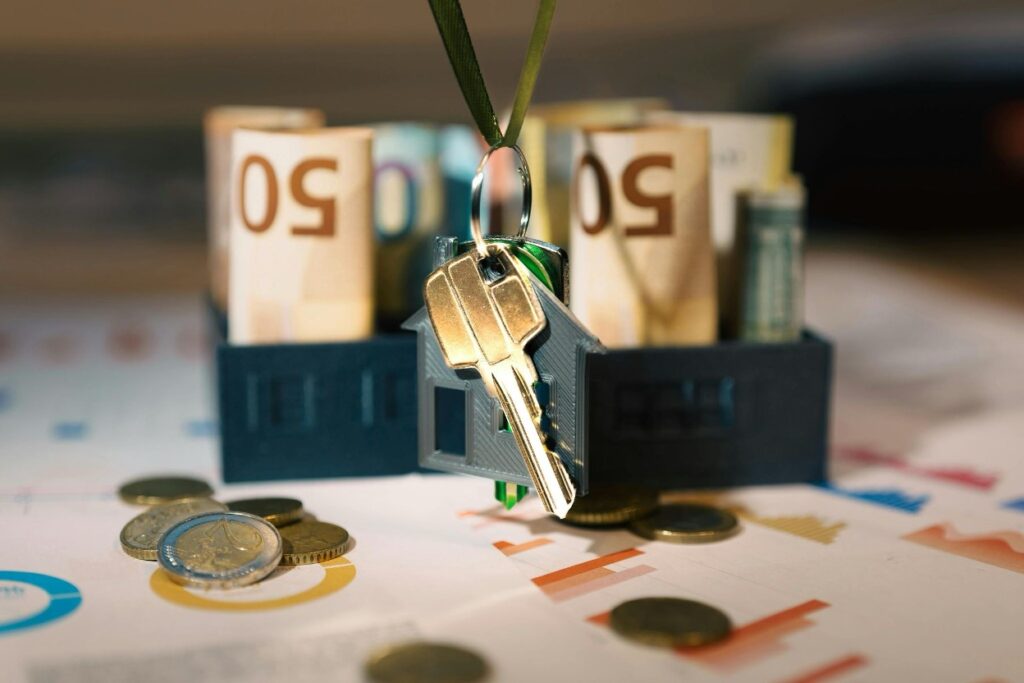 A house-shaped keychain resting beside rolled euro banknotes and coins
