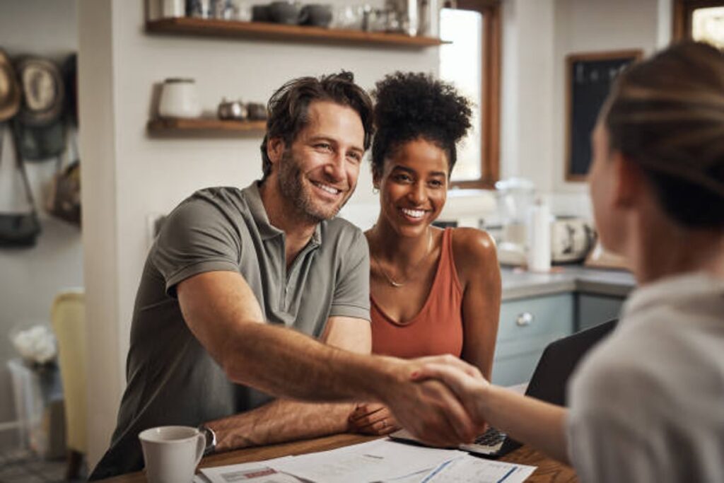 A smiling couple shaking hands with a financial advisor at their kitchen table, estate planning documents spread before them