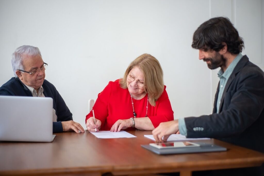 An older couple signing trust planning documents with an advisor at a table