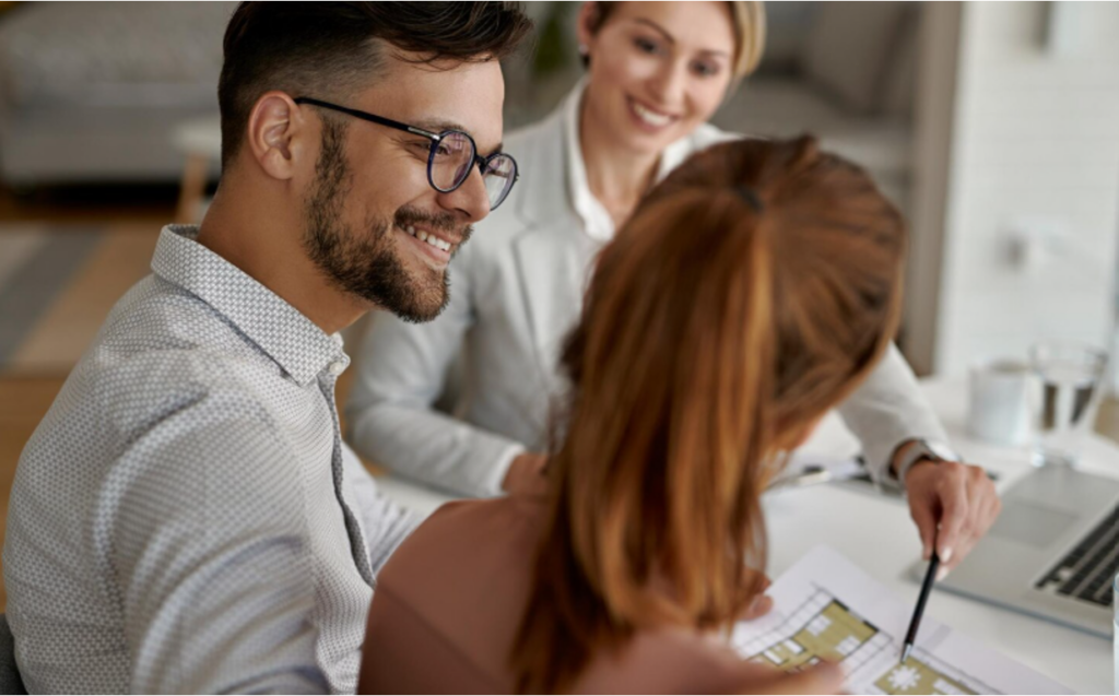 Young couple smiling while meeting with a real estate agent reviewing floor plans