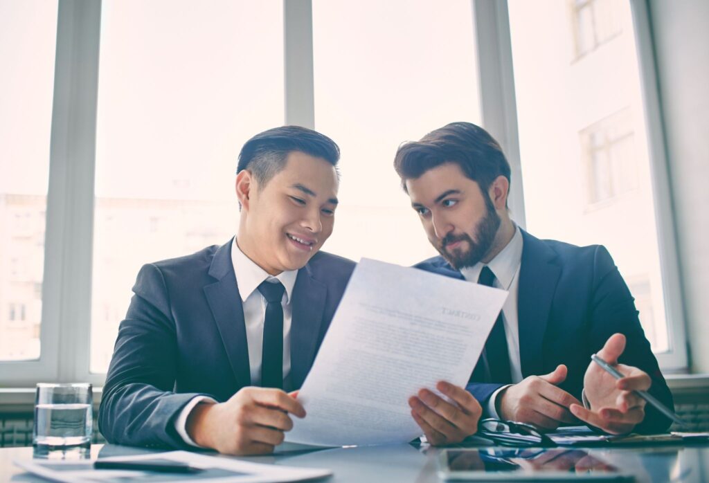 Two men in suits are reading a contract document together.