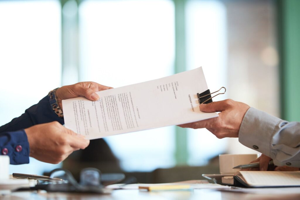 Two professionals exchanging a partnership agreement across an office desk. 