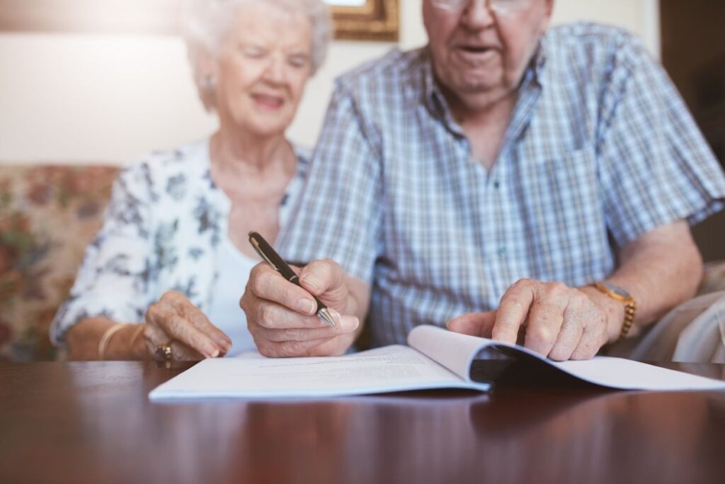 Senior couple signing estate planning documents together at home, reflecting a grantor trust review.