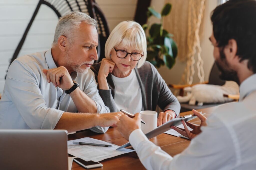 Older couple reviewing estate planning documents with a financial advisor across a wooden table.