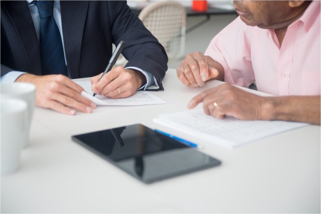 Two men signing a trust agreement document at a desk during a meeting. 